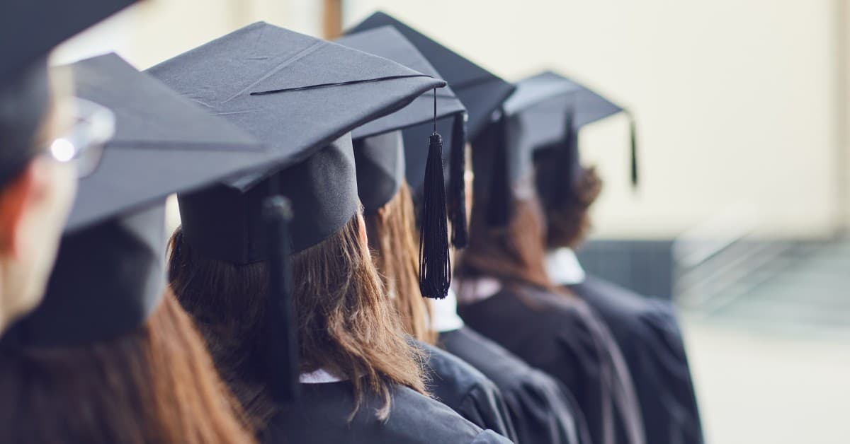A close-up view of a row of graduates. The students are wearing black gowns and mortarboards with black tassels.