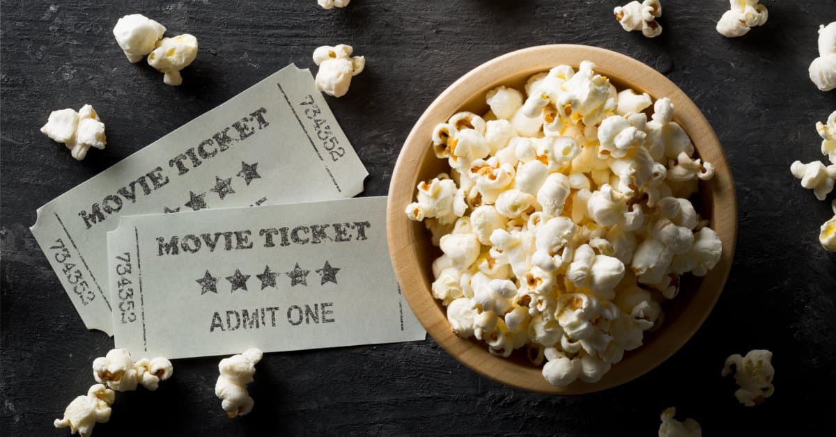 An overhead view of a bowl of popcorn and two movie tickets. Each ticket says "movie ticket" and "admit one" on the front.