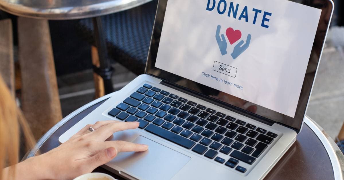 A close-up of an open laptop. The screen says "donate" and has a picture of a heart surrounding by two hands.