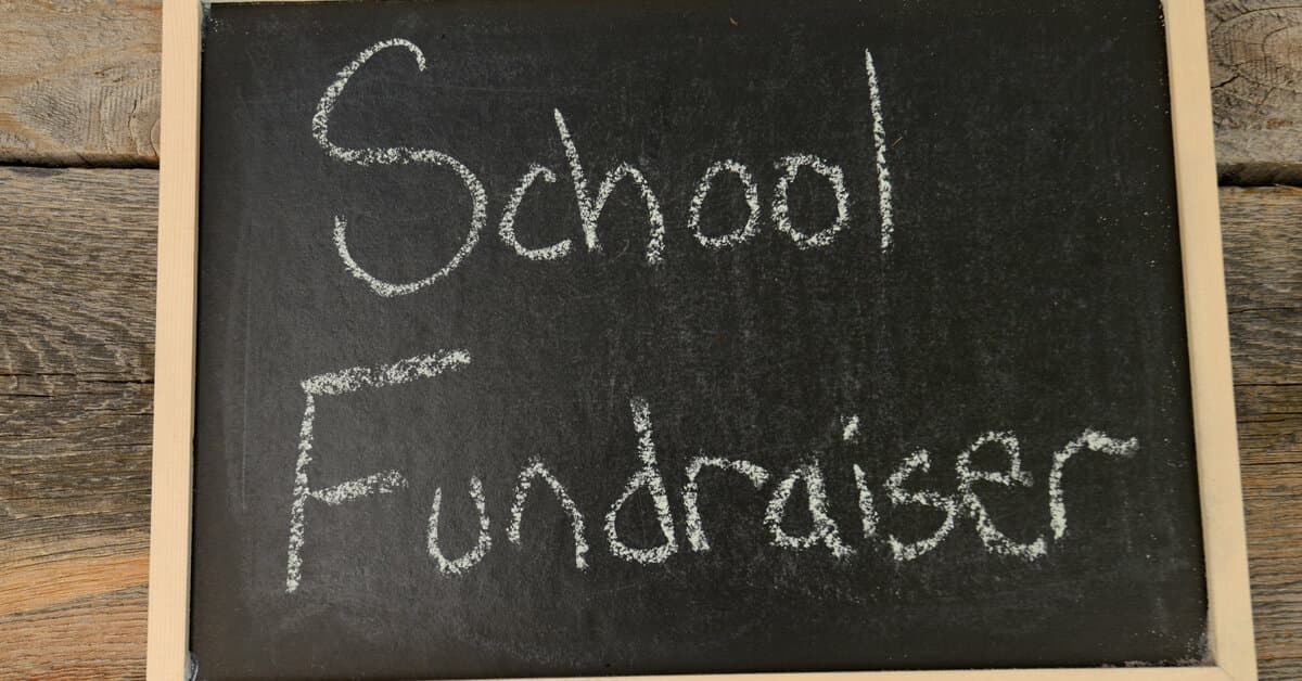 A rectangular chalkboard is resting on a wooden surface. The board says "School Fundraiser" in white chalk.