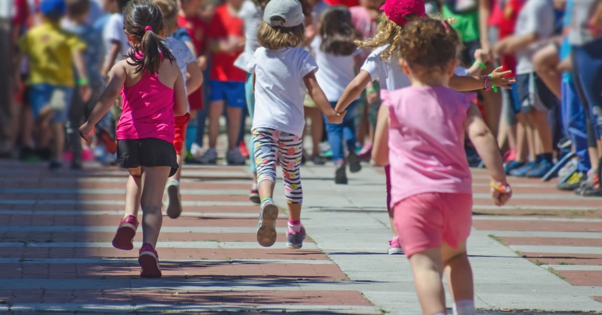 A group of young boys and girls wearing warm weather clothing while running outside toward a group of people.